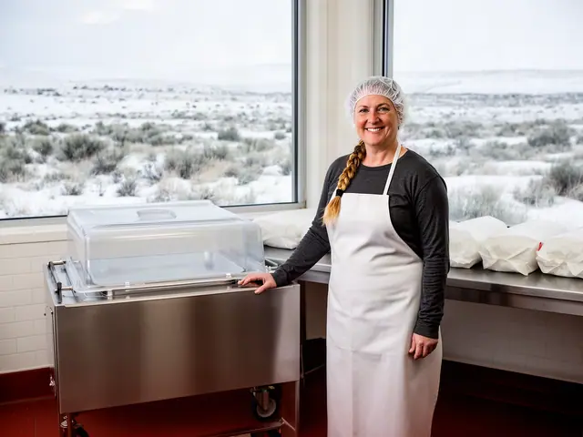 Smiling woman in a hairnet and white apron resting a hand on a stainless vacuum sealer beside wrapped loaves